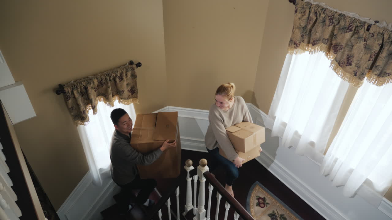 젊은 다민족 부부는 물건 상자를 계단 위로 운반합니다.