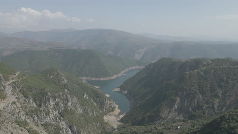 Drone-shot-flying-over-the-mountains-near-the-Koman-lake-in-Albania-on-a-sunny-day-with-clouds-with-blue-water-and-a-green-valley-LOG