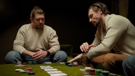 camera focuses on two men playing poker with friends