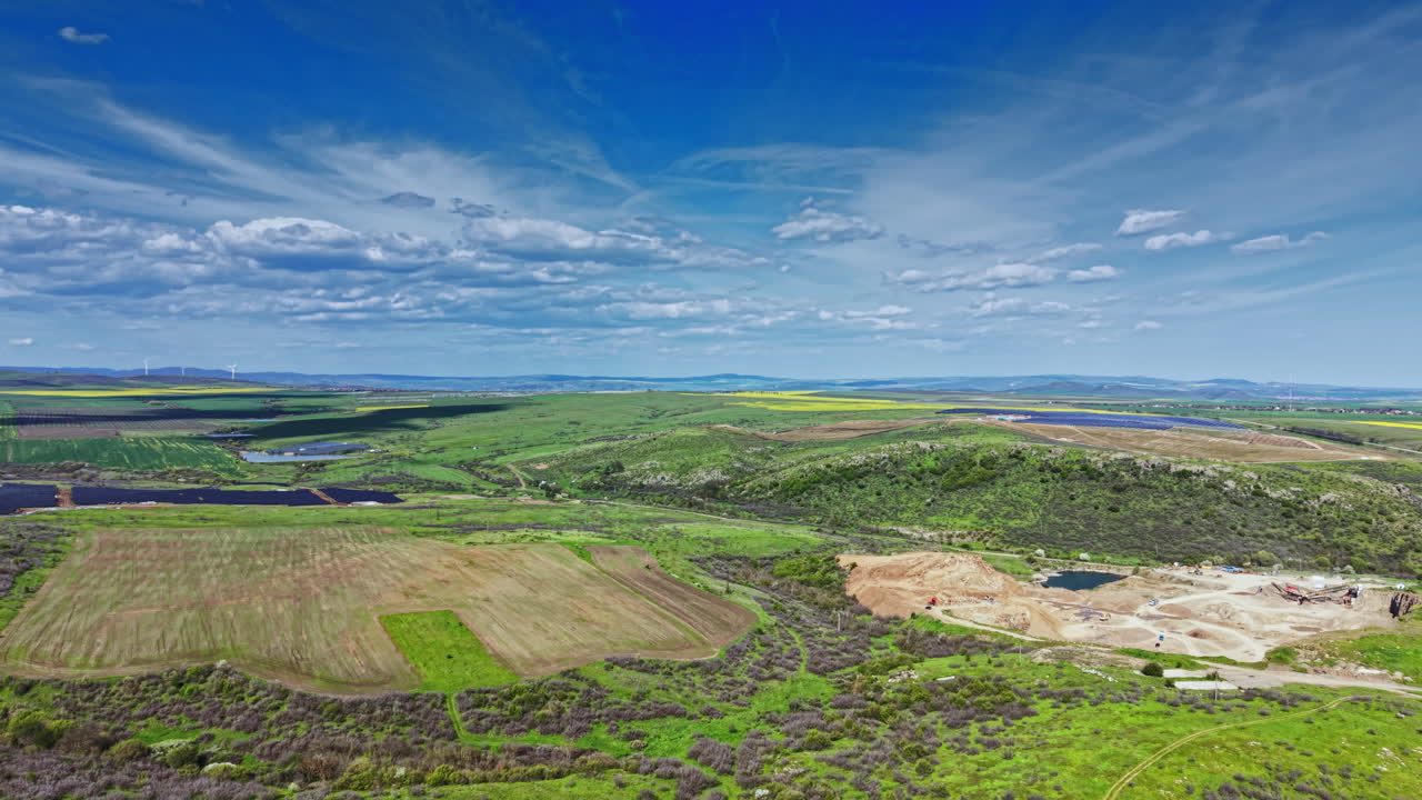 Udsigt over grønne marker og blå himmel over et landligt landskab med skyer og fjerne bakker sidst på eftermiddagen.