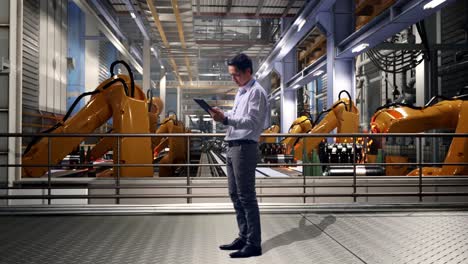 full body side view of an asian male professional worker standing with his tablet with industrial robotic arms working, working continuously with his tablet