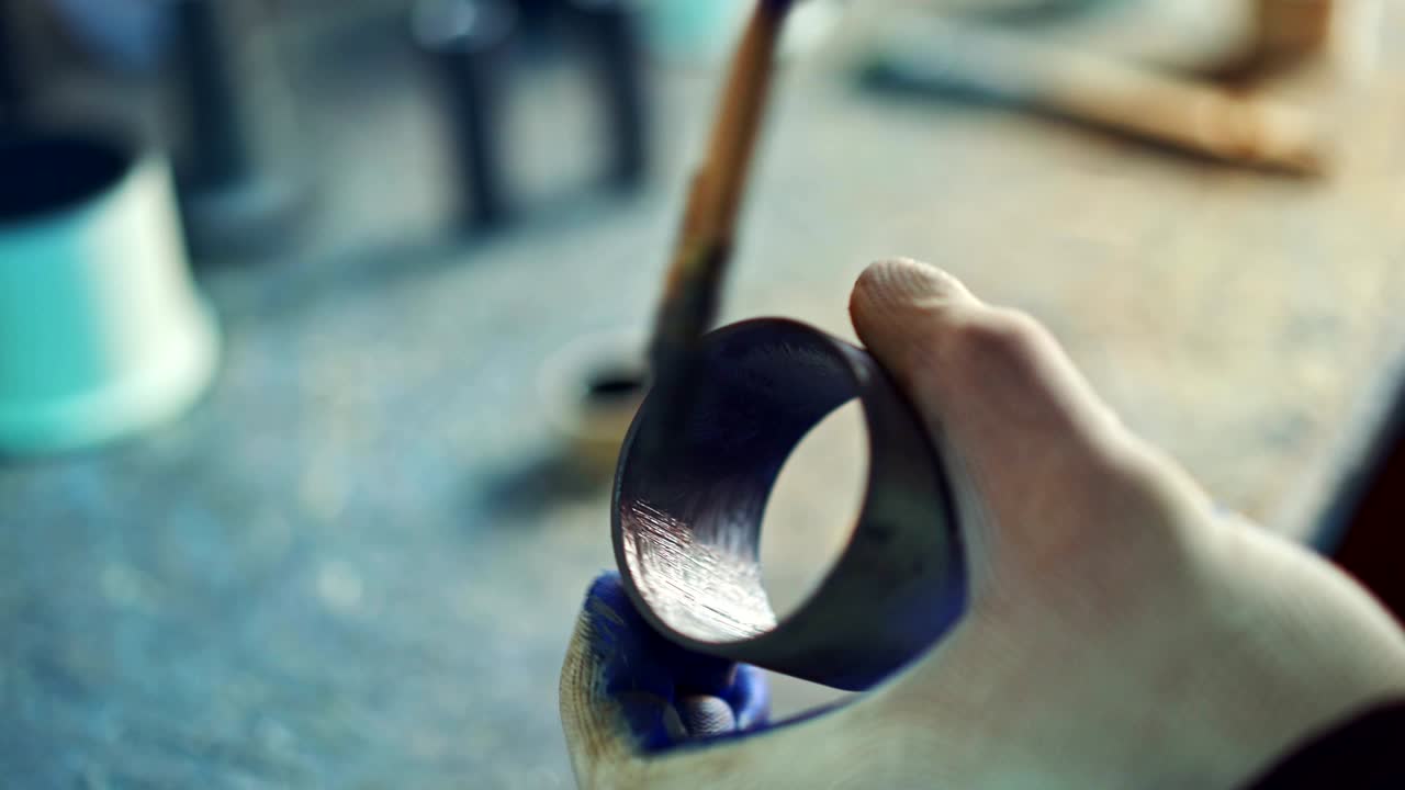 un hombre sostiene un rodamiento de bola en su mano y lo colorea en el interior usando un pincel en la fabricación.