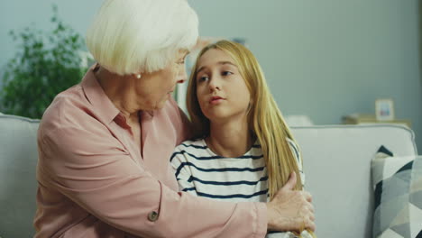 portrait shot of the cute teenage girl being upset while sitting on the sofa at home and her grandmother consolling and hugging her