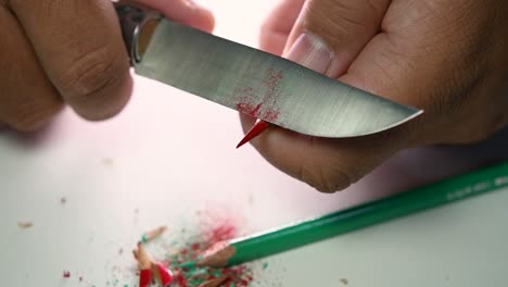 imágenes de manos afilando lentamente un lápiz y algunos lápices de colores con un cuchillo afilado