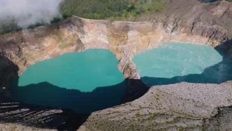 an aerial view shot of blue volcanic crater lakes on a hilltop with a forest