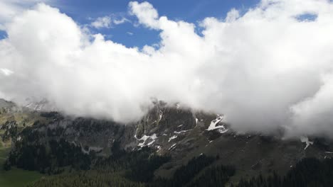 Fronalpstock-Glarus-Switzerland-aerial-with-fluffy-white-clouds-popping-above-the-mountains