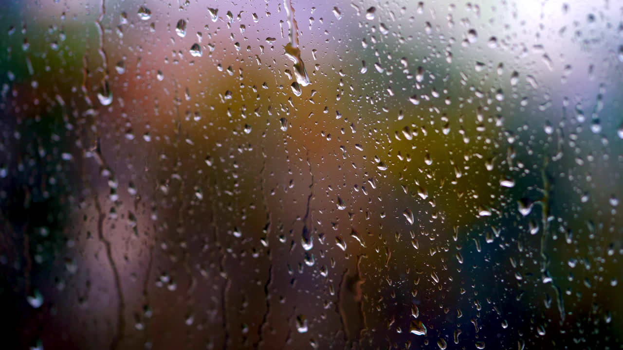 Heavy rain falling outside the window. Big drops moving down on glass background. Texture of flowing droplets on window. Close-up.