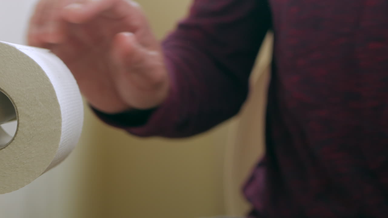 남자는 벽에 걸려 있는 두루마리에서 화장지를 꺼낸다
