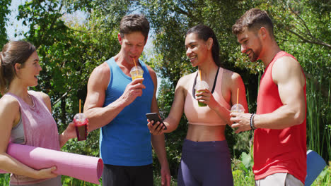 happy diverse group of men and women with health drinks laughing after yoga class in sunny park