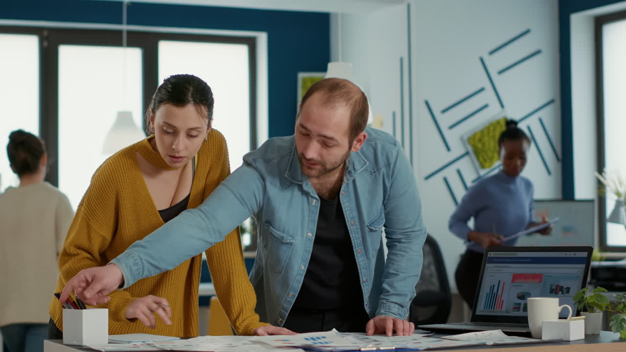 hombre en una oficina de puesta en marcha explicando gráficos de ventas y estadísticas a una compañera de trabajo tomando notas