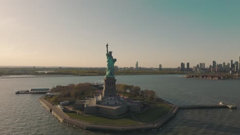 aerial of statue of liberty under the hazy sunset sky, new york skyline buildings in background, usa