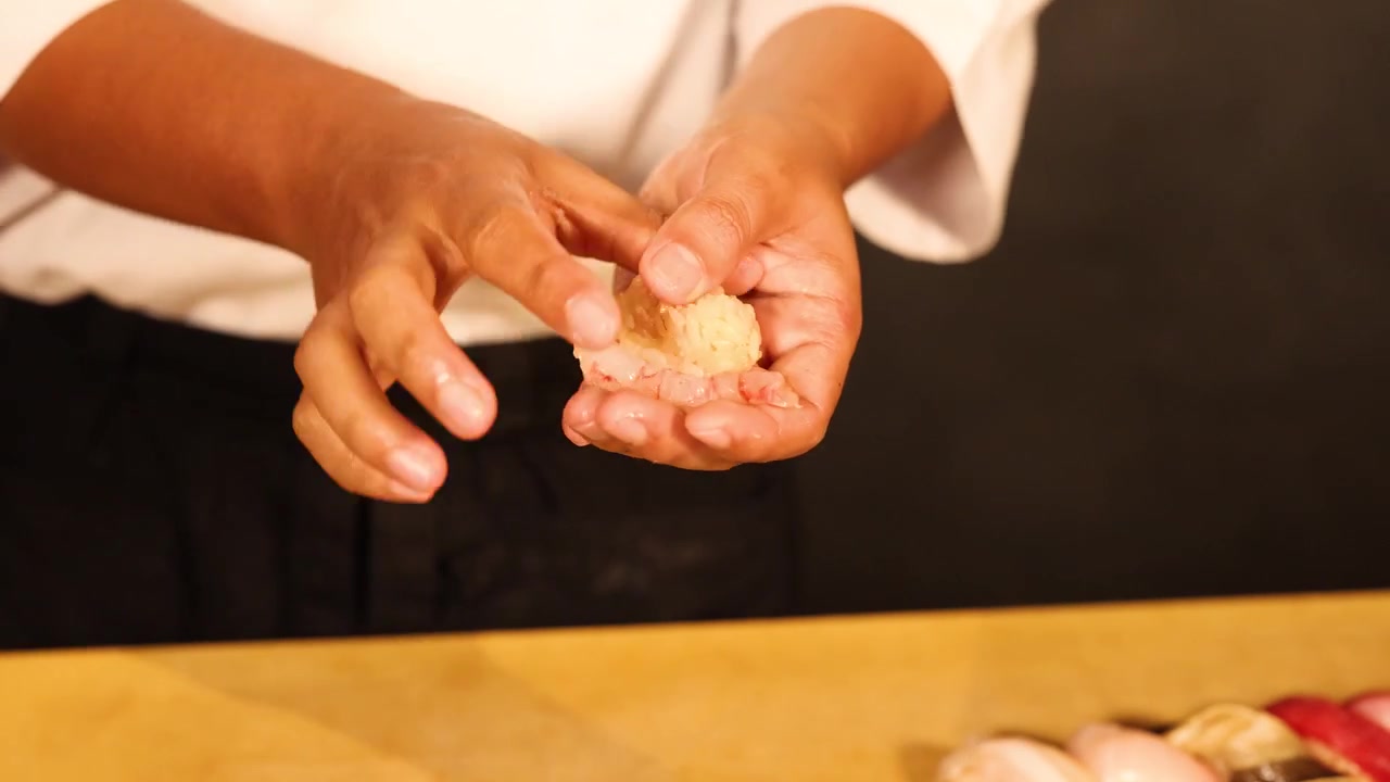 Close-up of a chef's hands shaping raw shrimp sushi with precision in Bangkok, Thailand.