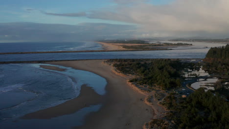 Drone-flying-backwards-over-Bastendorff-Beach-near-Coos-Bay-and-Shore-Acres-in-Oregon-during-sunset,-showing-entrance-to-harbor