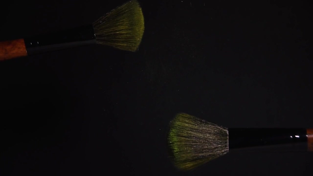 slow motion of two make up brushes with yellow powder explosion and burst on black background