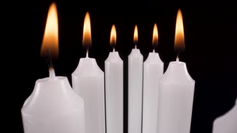 macro view flying past lit candles on black background, moving past white candles