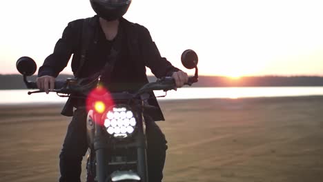 close up of biker's ride on black sport bike with switched front headlight. waterfront, sunset