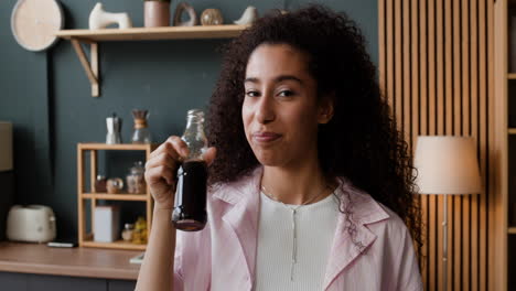 young woman drinking and presenting a beverage in her kitchen