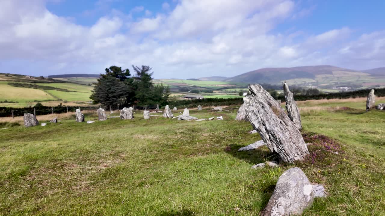 Ancient stone circle ruins standing in green rural landscape under blue sky