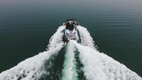 overhead drone view of a wakeboarder hugging the wake on one side of a fast-moving speedboat on a sunny day