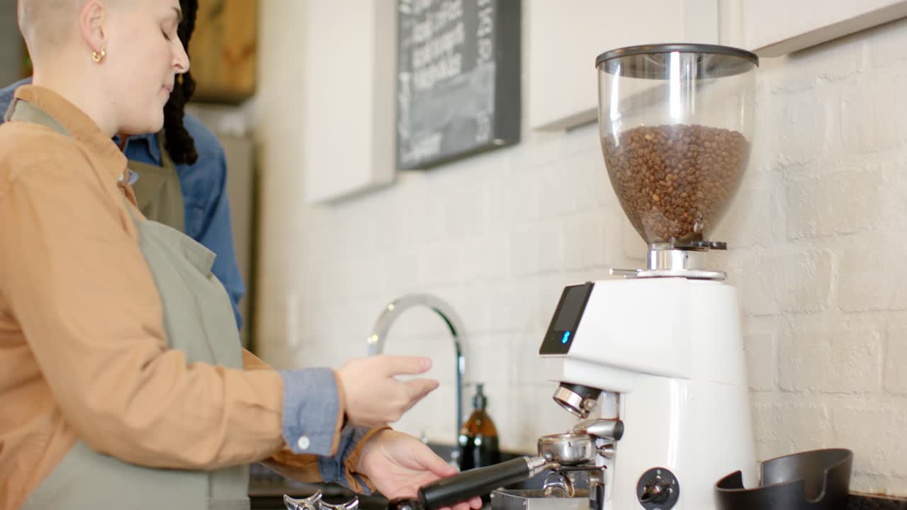 Diverse coworkers gesturing at cafe grinder, filling portafilter with guidance for espresso grounds