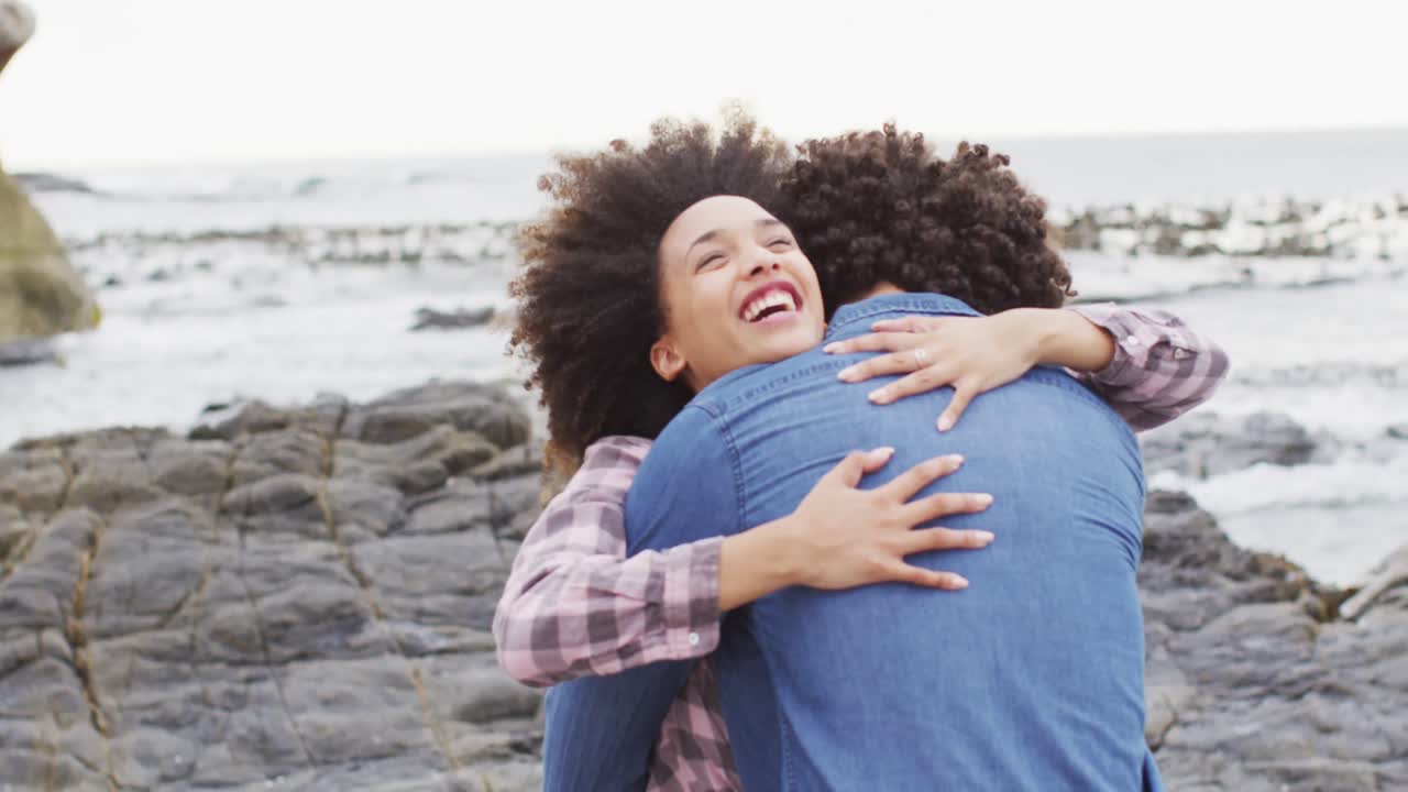 African american woman hugging her husband on the rocks near the sea
