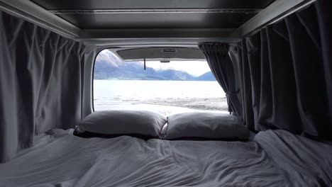 slowmo - interior of motorhome bed with pillows and blankets by lake wakatipu, queenstown, new zealand with snowcapped mountains in background