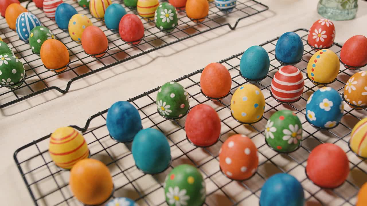 Shifting camera revealing hand-decorated eggs on wire racks at home table, bringing jar into view