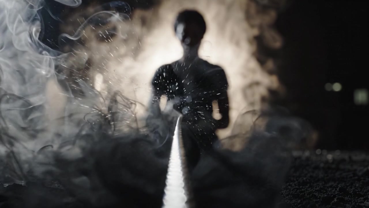 Una figura solitaria che lavora artisticamente con strumenti, circondata da fumo enigmatico e ombre, creando un'atmosfera accattivante in un ambiente scarsamente illuminato.