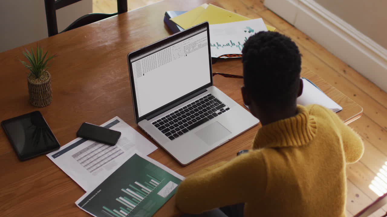 African american man sitting at desk watching coding data processing on laptop screen