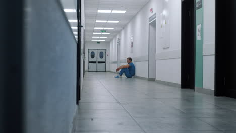 stressed doctor sitting leaning on wall hallway. tired medical worker resting.