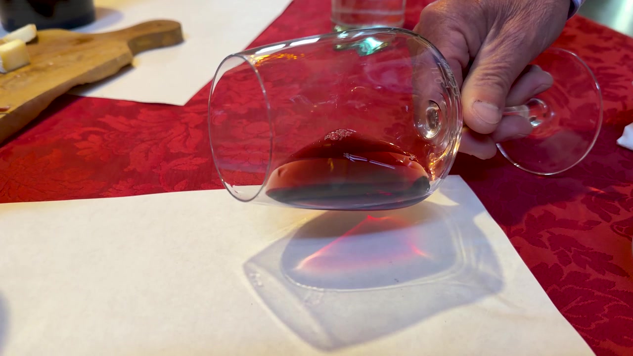 Une main fait tournoyer du vin rouge dans un verre au-dessus d'un papier blanc pour l'évaluation de la couleur