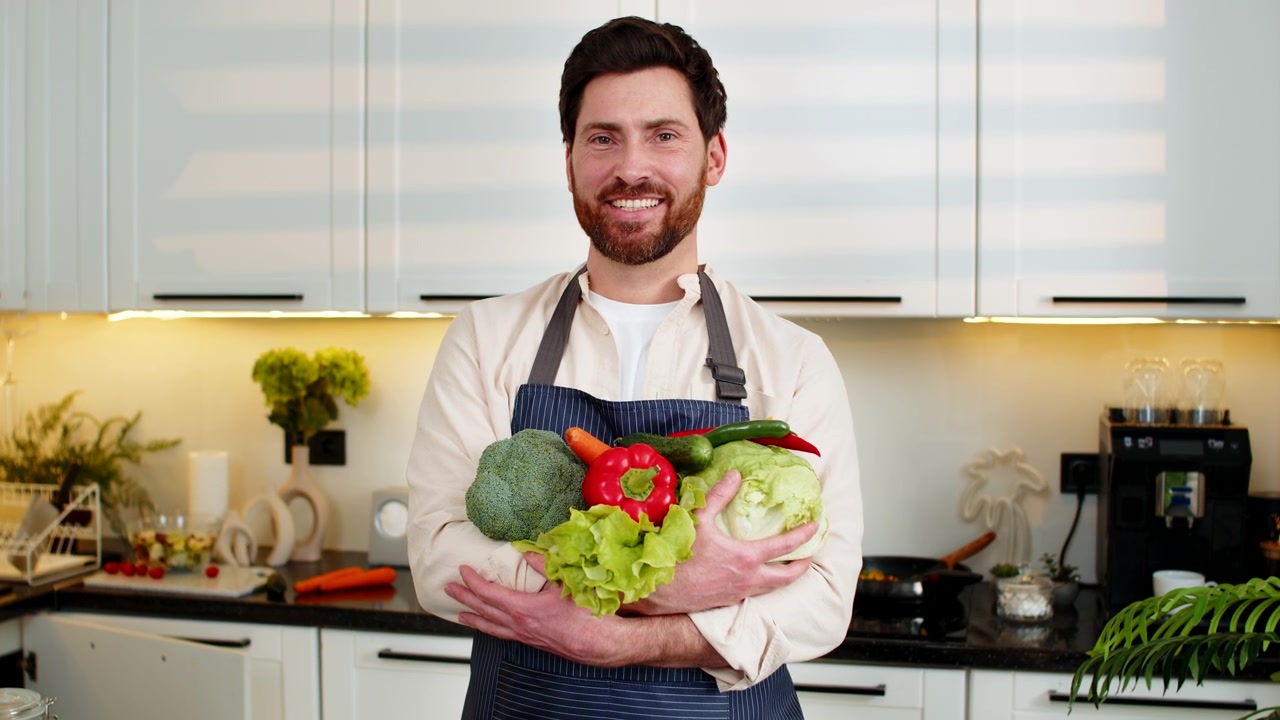 Uomo di mezza età che tiene in mano verdure fresche nella cucina di casa, sorridente per la preparazione di un pasto salutare