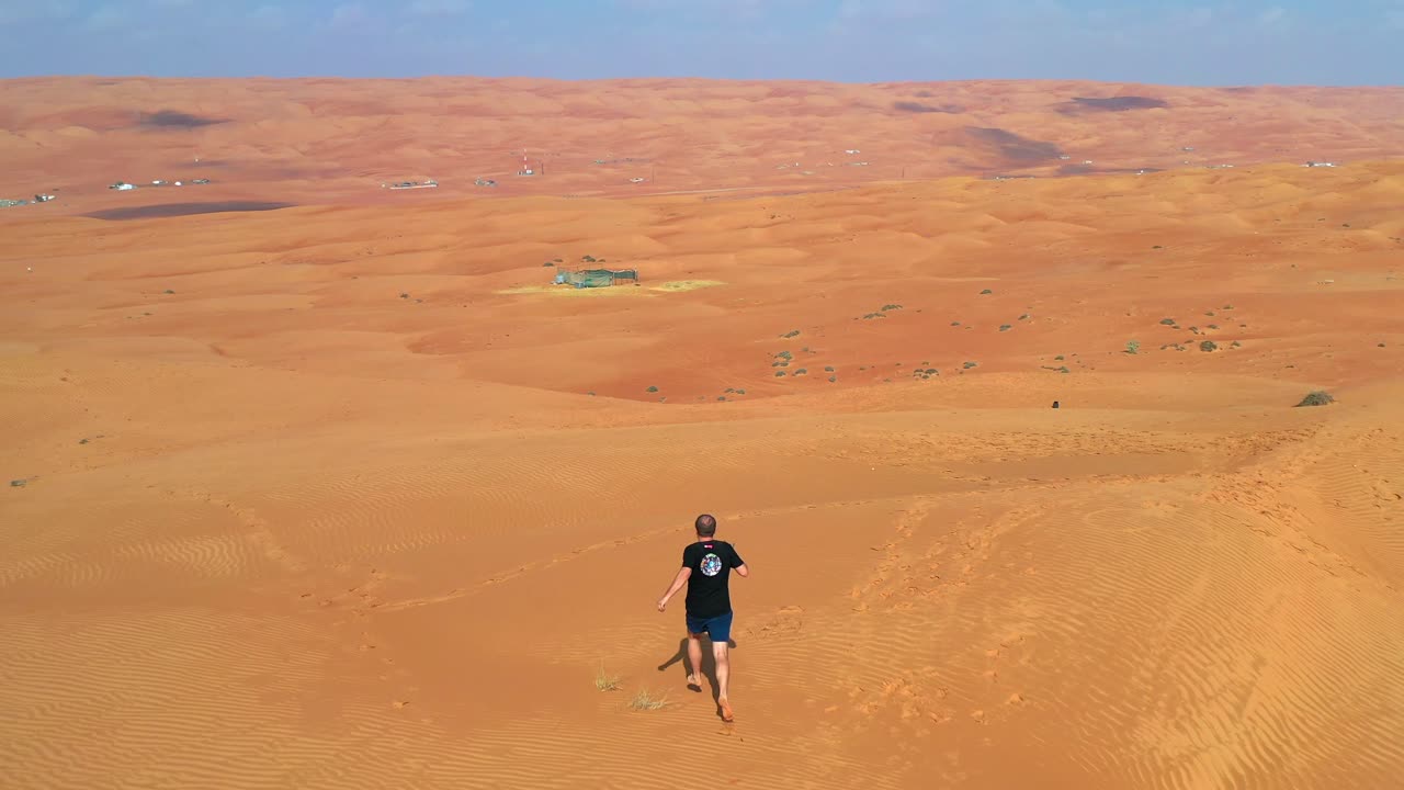 드론 컨트롤러를 손에 들고 끝없이 광활한 황량한 사막의 모래 위를 맨발로 달리는 남자