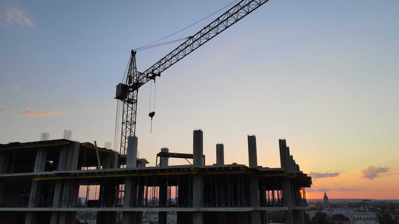 grúa de elevación de torre y edificio de apartamentos residenciales altos con marco monolítico en construcción al atardecer. desarrollo inmobiliario