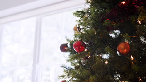 Downwards-tilt-shot-from-the-top-of-a-decorated-Christmas-tree-in-front-of-a-window