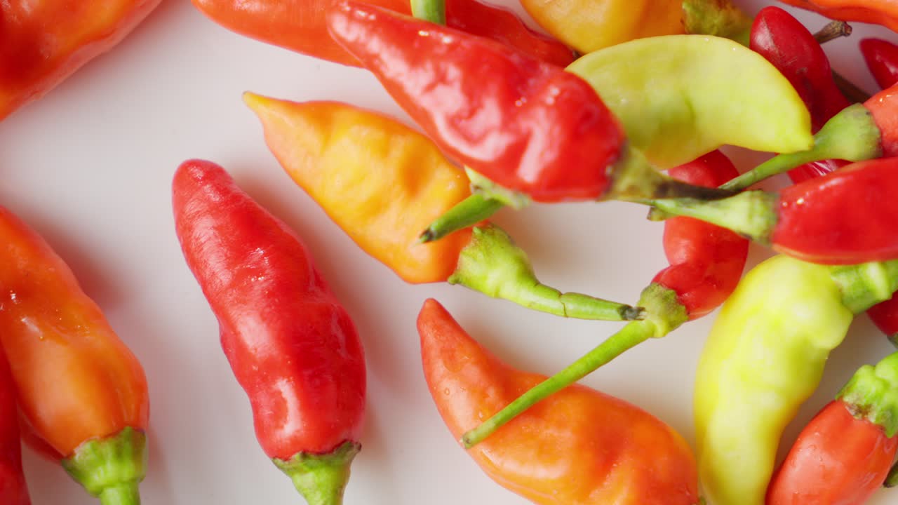 chiles indonesios vibrantes en varios colores caen, esparcidos en una superficie blanca, tomada de cerca