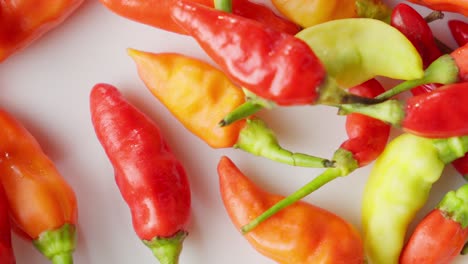 vibrant indonesian chilis in various colors drops, scattered on a white surface, close-up shot