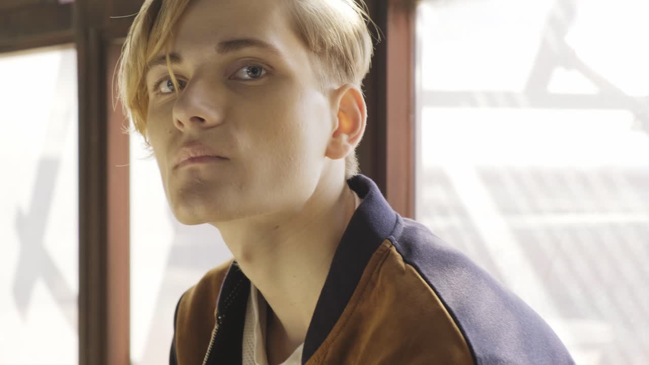 молодой человек сидит возле окна в старой комнате.