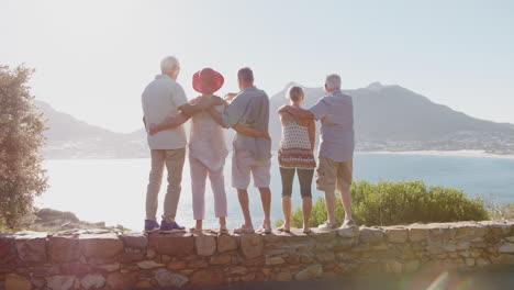 Rear-View-Of-Senior-Friends-Visiting-Tourist-Landmark-On-Group-Vacation-Looking-Out-At-Bay