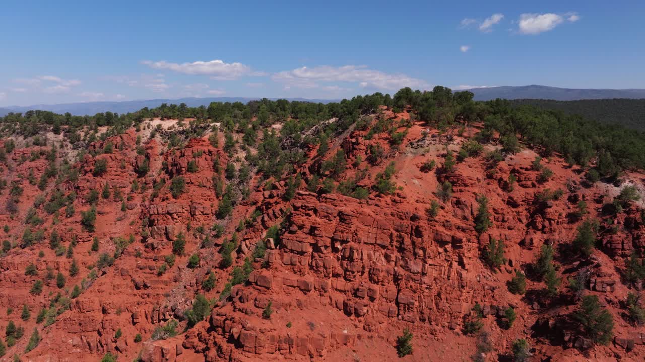 Rugged red cliffs encircle green pockets of vegetation around Mushroom Rock under clear sunlight, aerial descend estabilsh, Carbondale Colorado