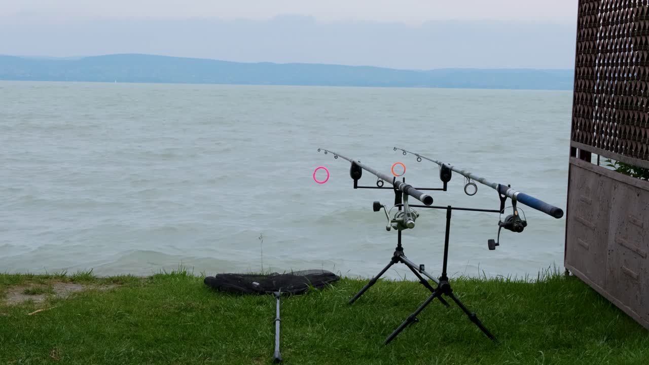 Bite indicator on the fishing rod moving at lake in cloudy and windy weather