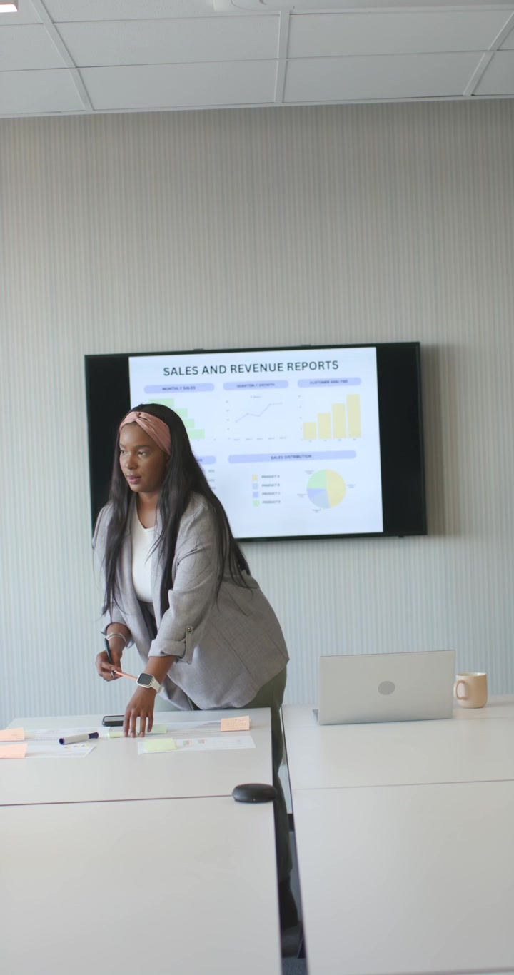 Video verticale: Donna africana che controlla gli appunti, si sposta al tavolo e sistema i post-it per una slide di vendita.