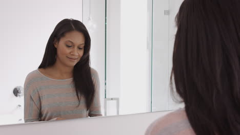 woman looking at reflection in bathroom mirror brushing teeth