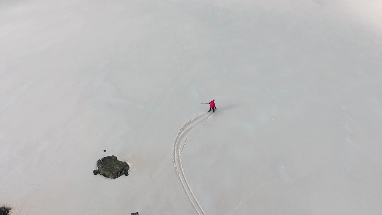 Vista aerea di uno sciatore con una giacca rossa su una montagna innevata.