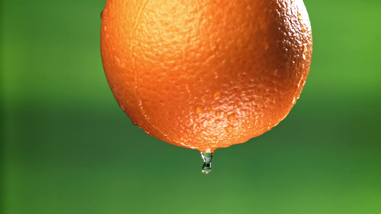 Vand drypper fra en våd appelsin i slowmotion
