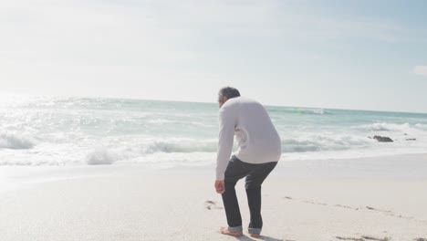 back view of hispanic senior man sitting on beach at sunset