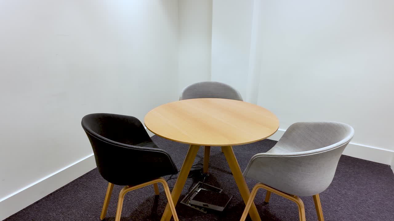 Mesa redonda pequeña con sillas en una sala de reuniones vacía para sesiones de colaboración e intercambio de ideas. Interior de oficina moderna con diseño minimalista y paredes blancas