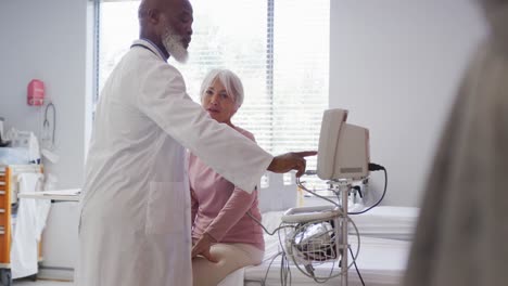 médico afroamericano de sexo masculino que muestra los resultados de una paciente caucásica senior en el monitor del hospital