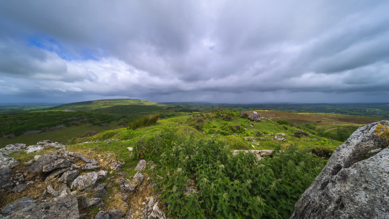 Timelapse af et landligt landskab med klippeformation i forgrunden og bakker i det fjerne under en forbipasserende regnbyge, set fra Carrowkeel i County Sligo i Irland.