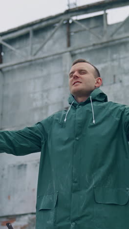 survivor breathing deeply in destructed place. man in protective suit holding safety gas mask in hands in enjoys fresh air on the background of ruined building. vertical video